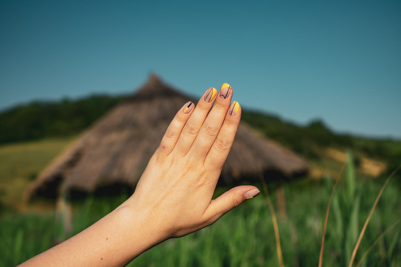 stats-img A close-up of a hand showcasing stylish nail art set against a rustic countryside background.