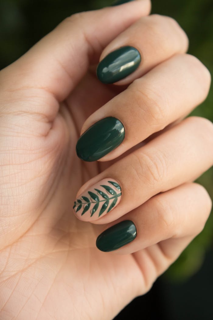 portfolio-01 Close-up of a stylish green manicure with a leaf design, showcasing glossy fingernails and natural skin tone.