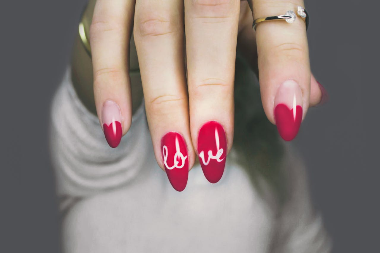 portfolio-06 Vibrant red nails with love art on a womans hand, showcasing elegant style and design.
